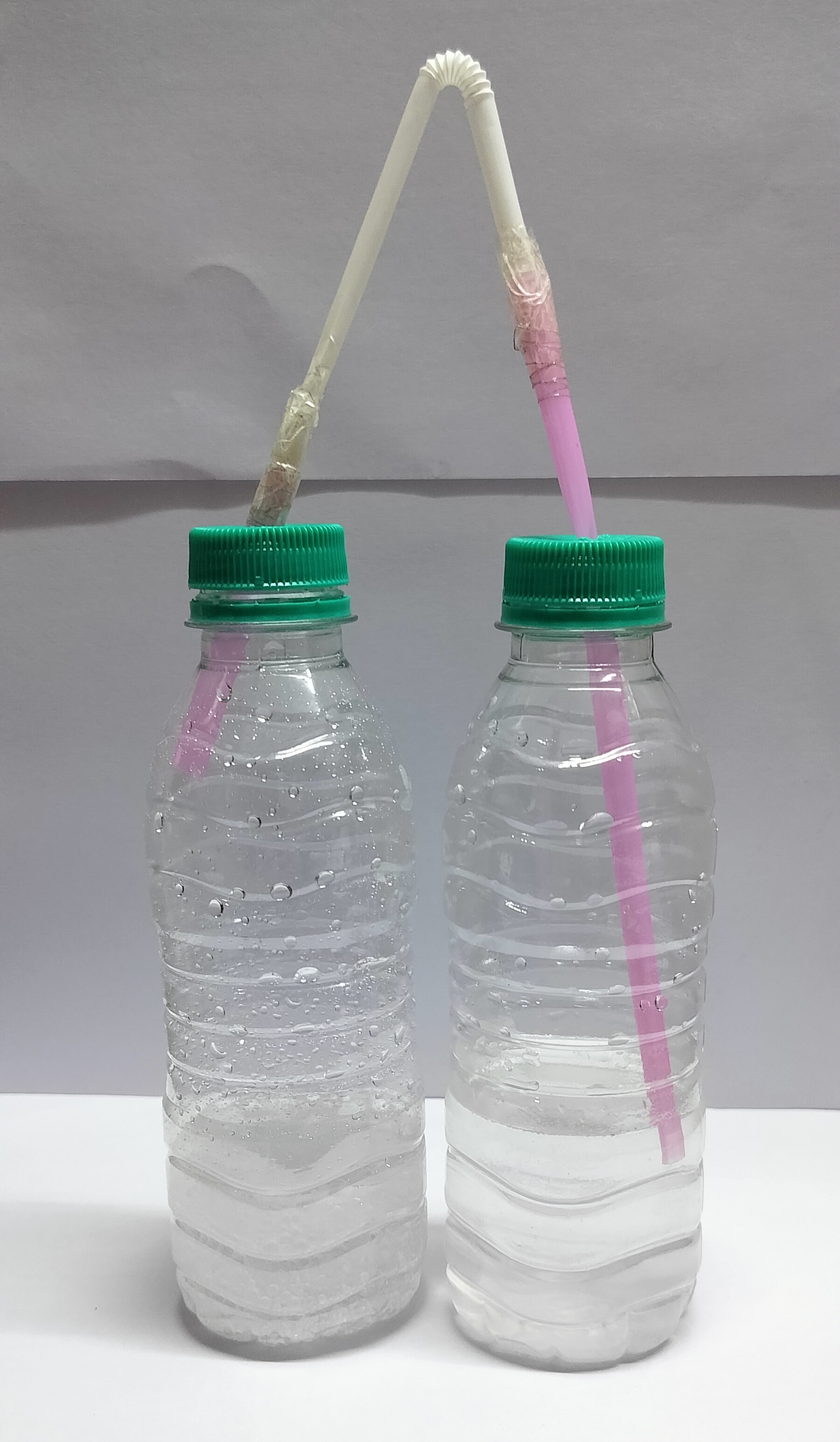 Image: Two-part figure showing the reaction of vinegar and baking soda; (a) a test tube setup with a delivery tube connecting one test tube containing vinegar and baking soda (with bubbles of carbon dioxide gas rising) to another test tube containing lime water; (b) the same setup performed with two used plastic bottles connected by a flexible straw